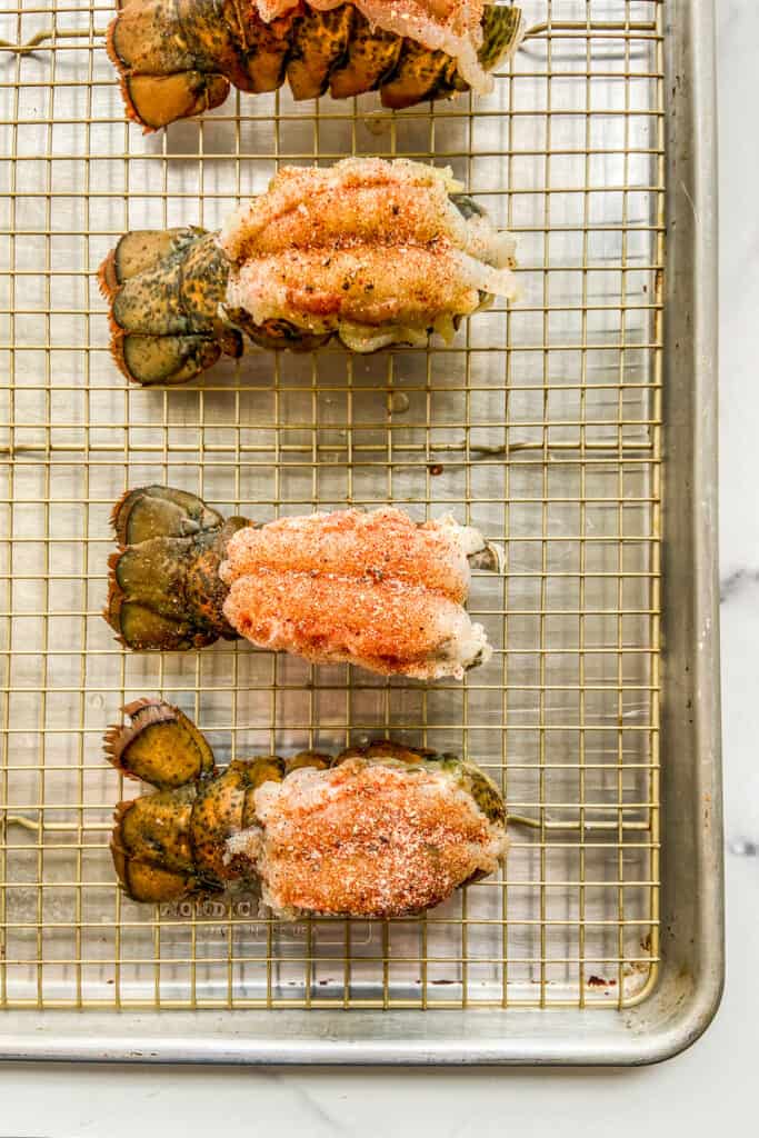 Lobster tails on a sheet pan, topped with spices.