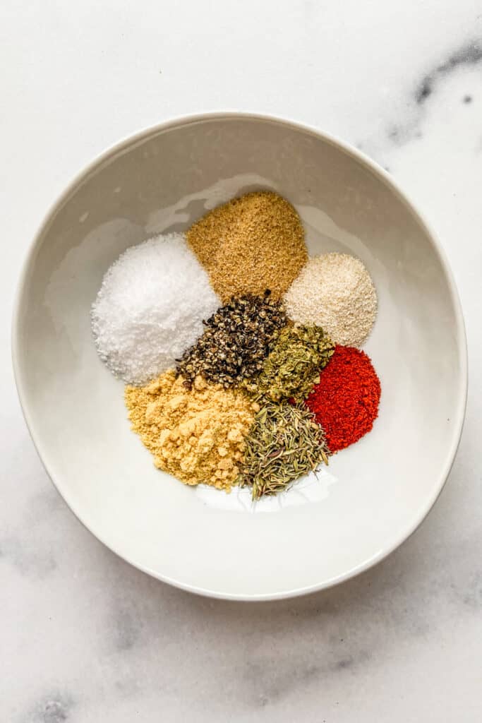 Spices and herbs for chicken seasoning blend in a small, white bowl.