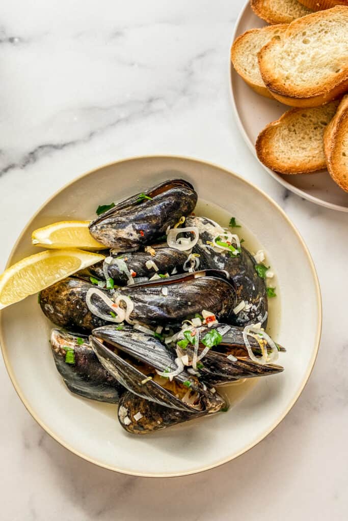 Drunken mussels in a bowl with a side of toasted bread.