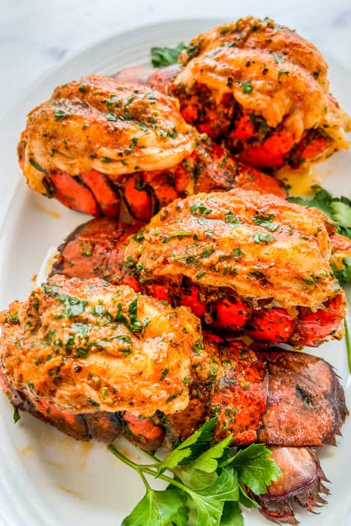 Four garlic butter topped lobster tails on a serving platter.