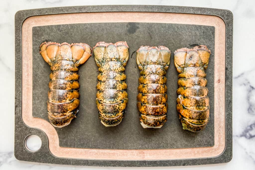 Four lobster tails on a cutting board.