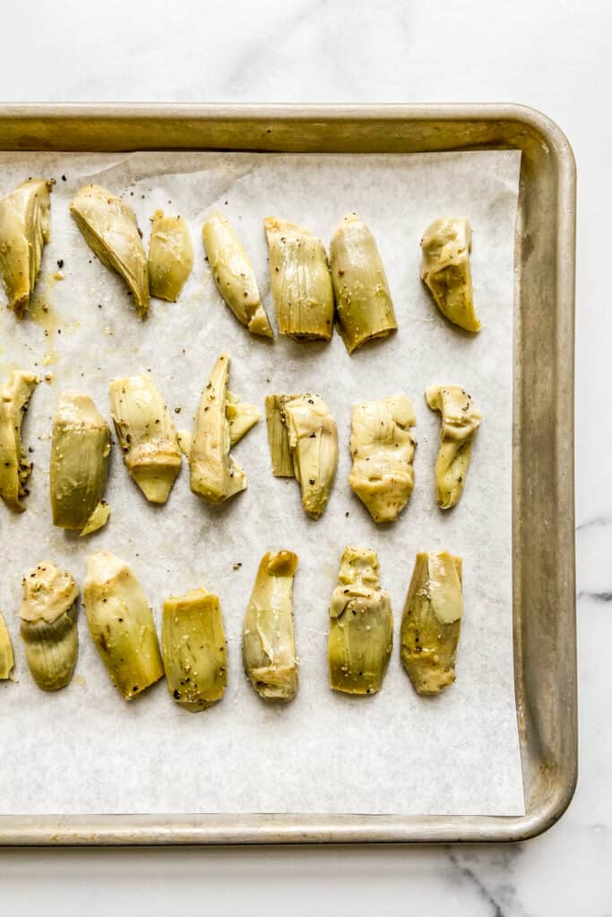 Artichoke hearts on a parchment lined baking sheet.