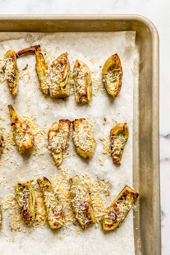 Parmesan topped roasted artichokes on a baking sheet.