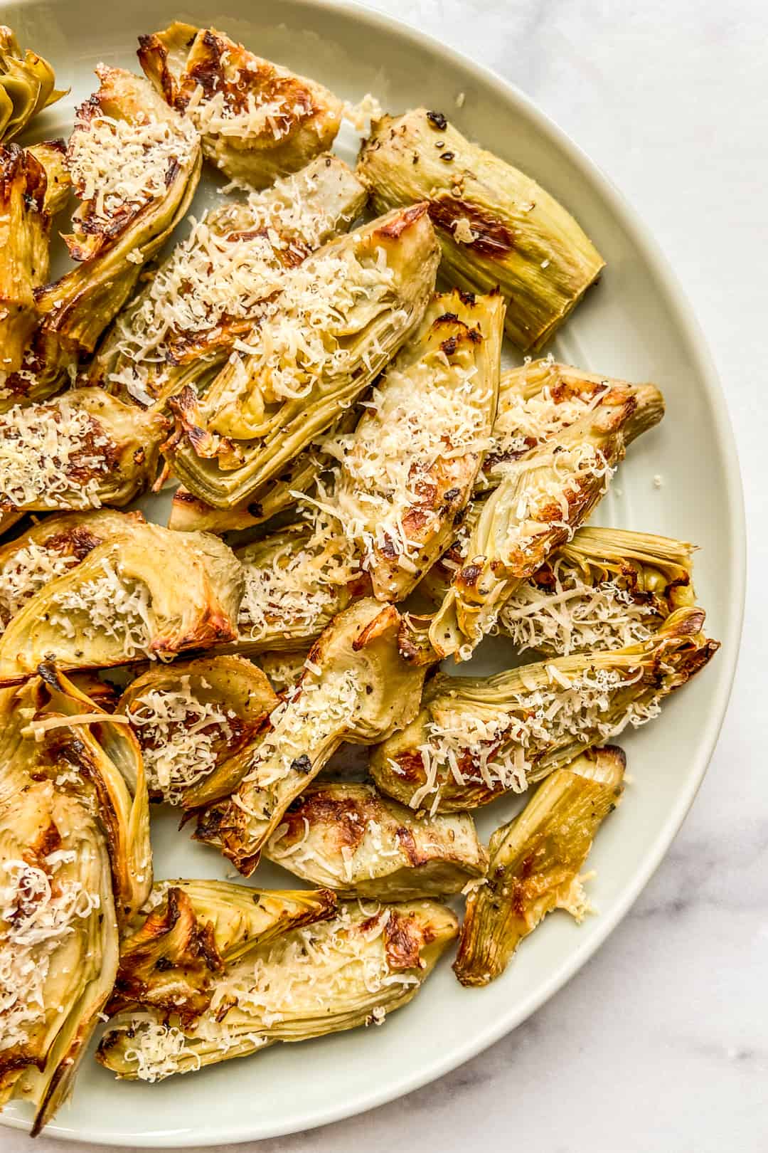 Roasted artichoke hearts topped with parmesan on a small green plate.