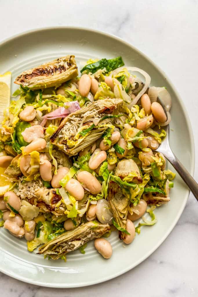 White bean artichoke salad on a green plate with a spoon.