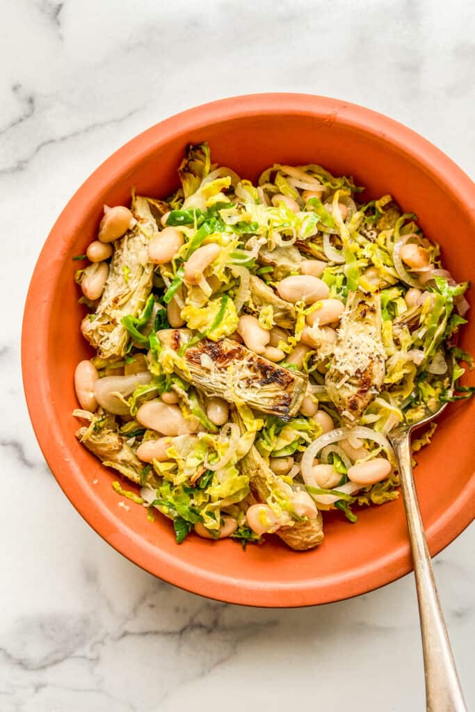 Roasted artichoke and white bean salad in a terracota colored bowl.