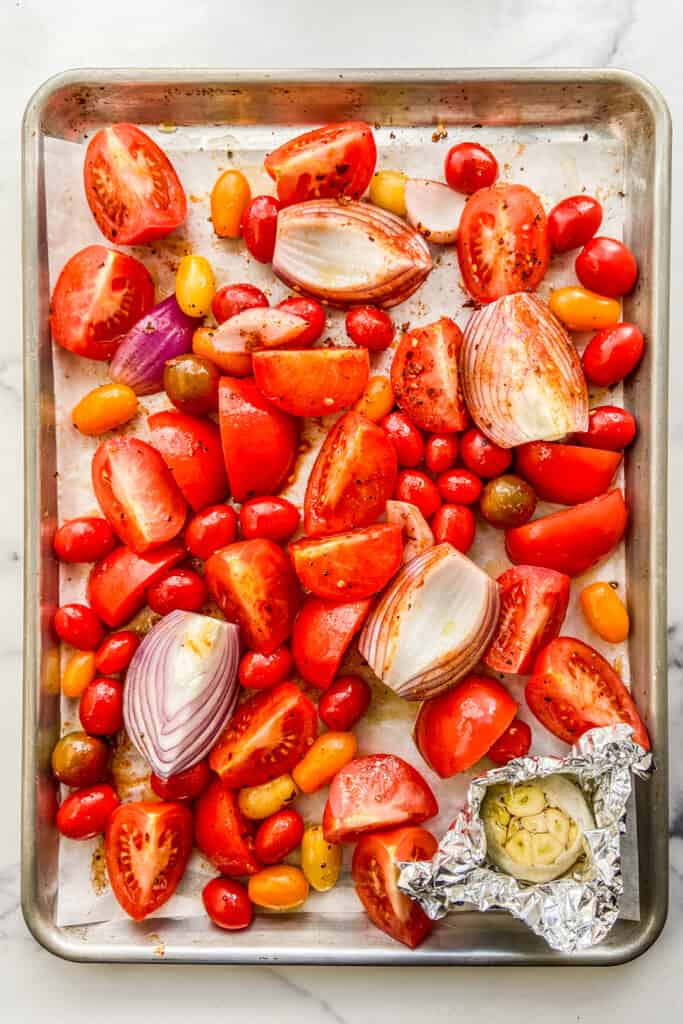Tomatoes, red onion, and garlic on a sheet pan.