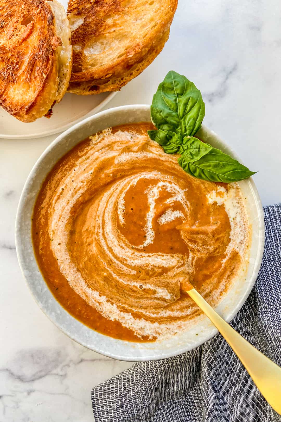 Roasted tomato soup with basil in a bowl with a gold spoon.