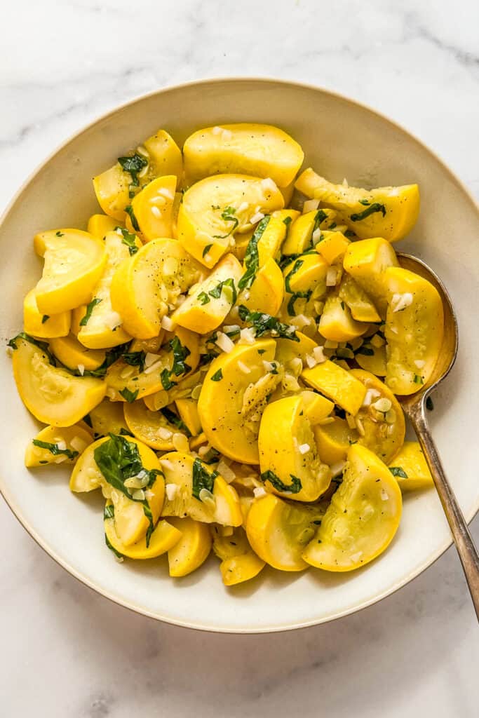 Sautéed yellow squash topped with herbs in a white serving bowl.