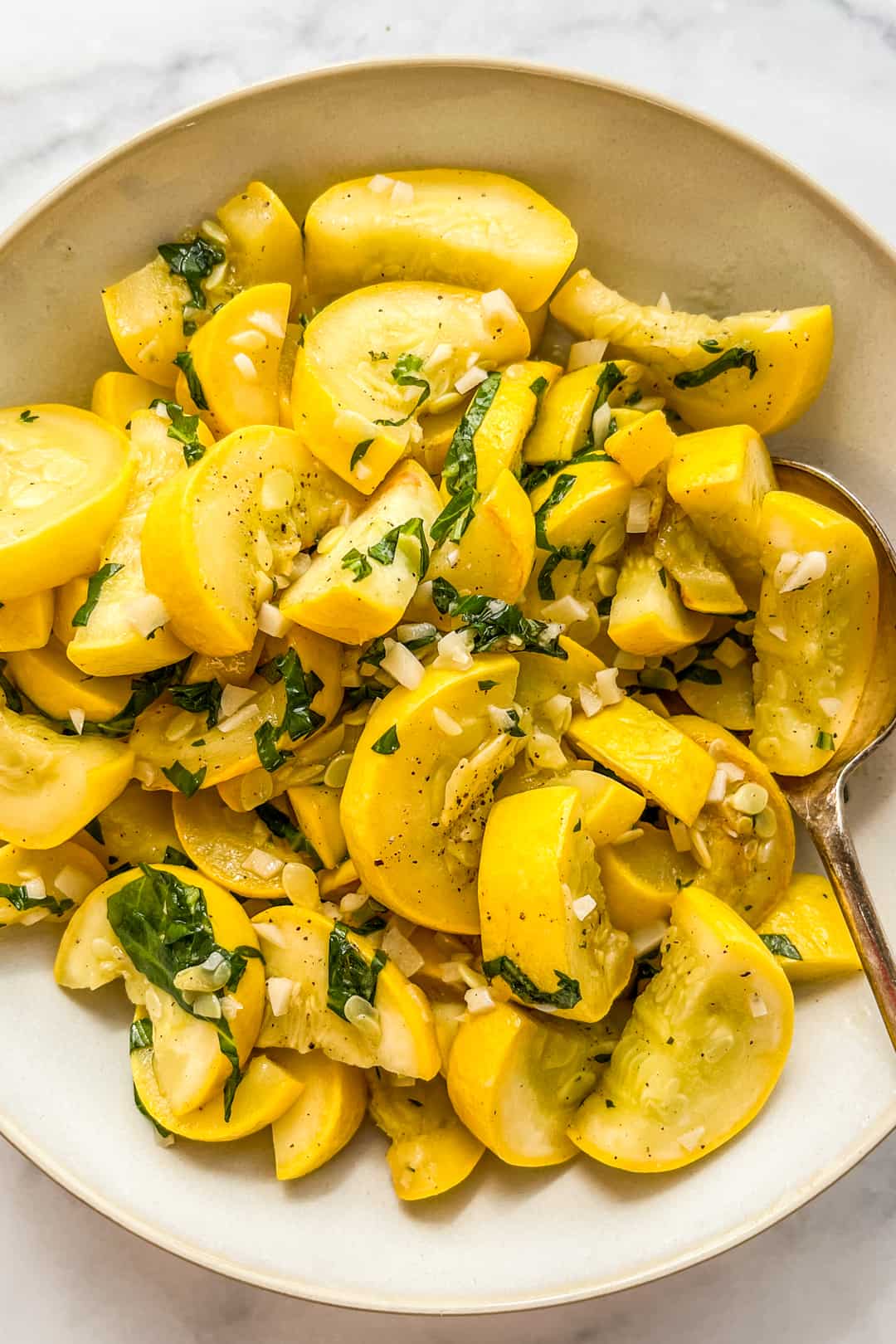 Sautéed yellow squash topped with herbs in a white serving bowl.