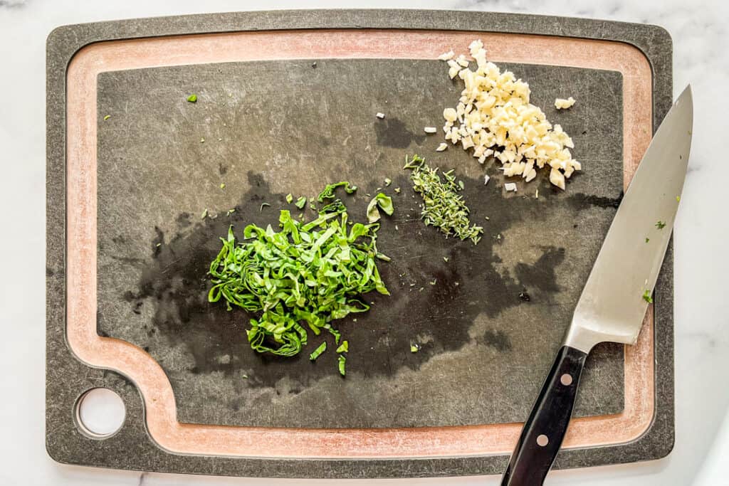 Chopped garlic, thyme, and basil on a cutting board.