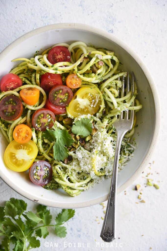 Spiralized summer squash with tomatoes in a white bowl with a fork.