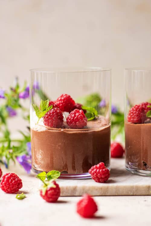 Vegan chocolate mousse topped with raspberries in a glass cup.