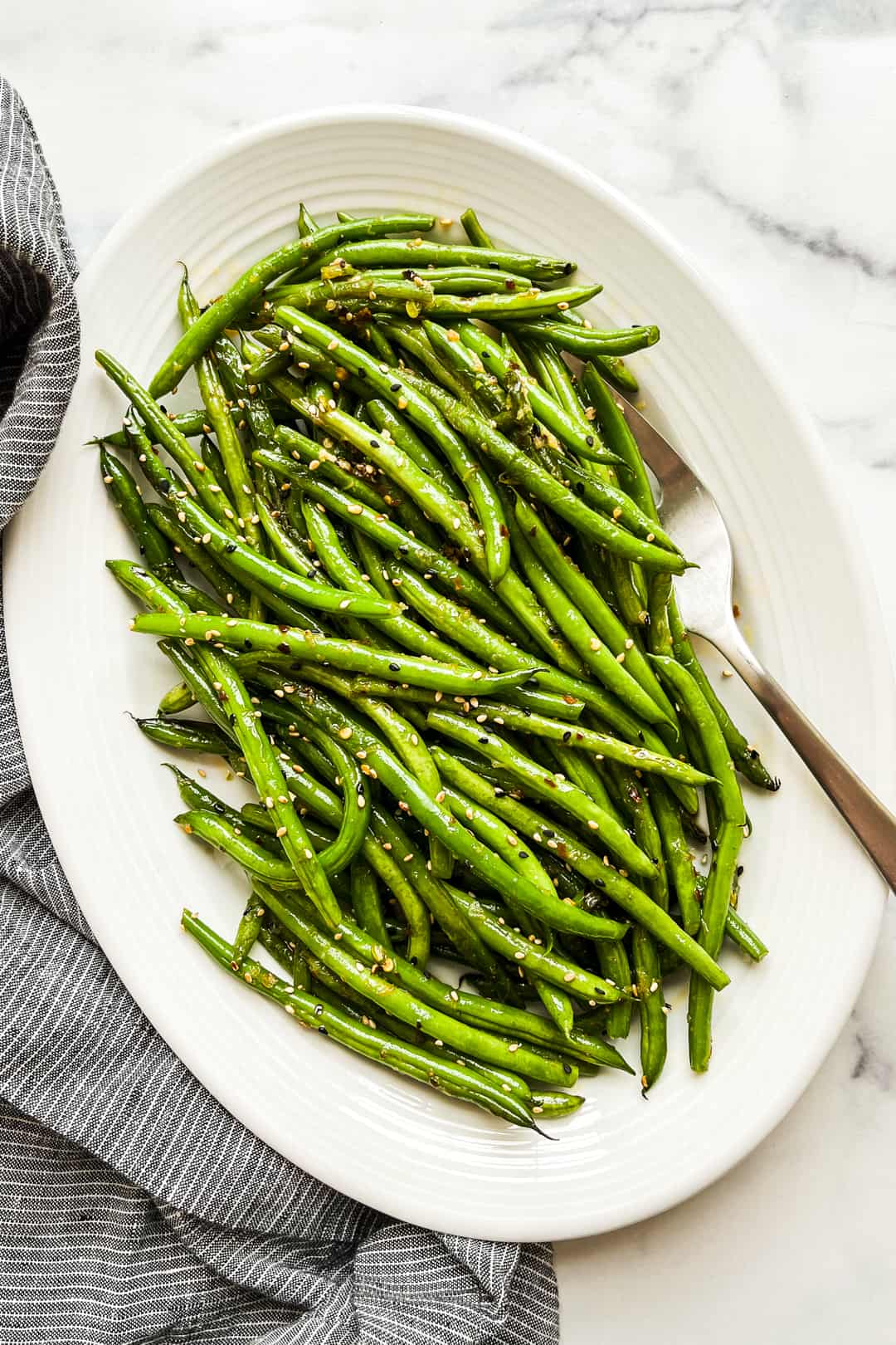 Asian green beans on a white platter with a silver serving fork.