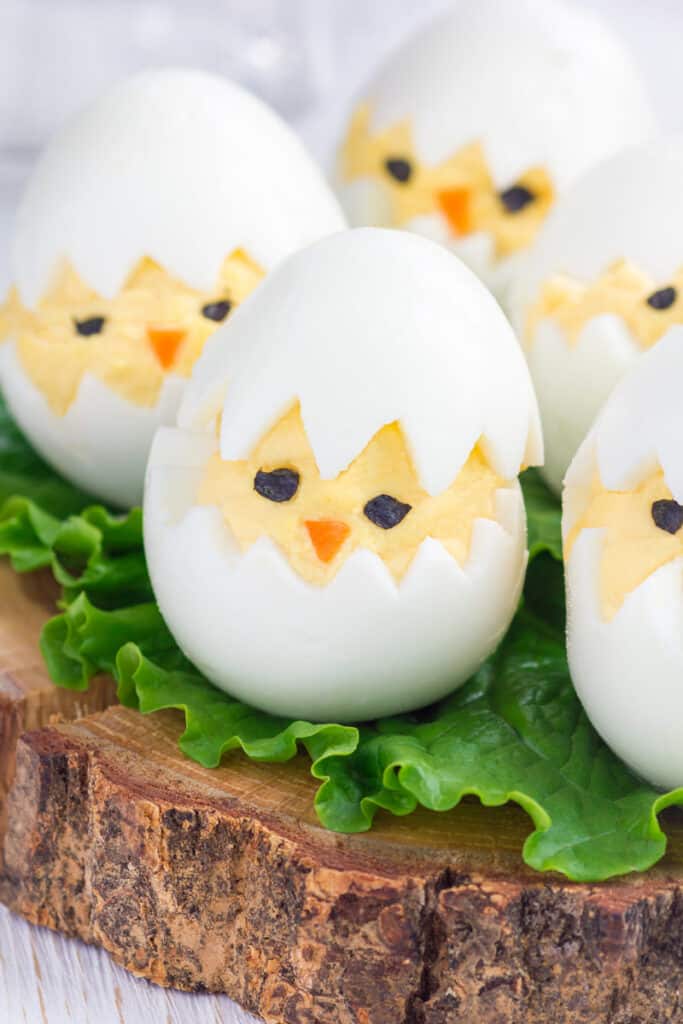 Deviled egg chicks on a piece of lettuce on a plate of wood.