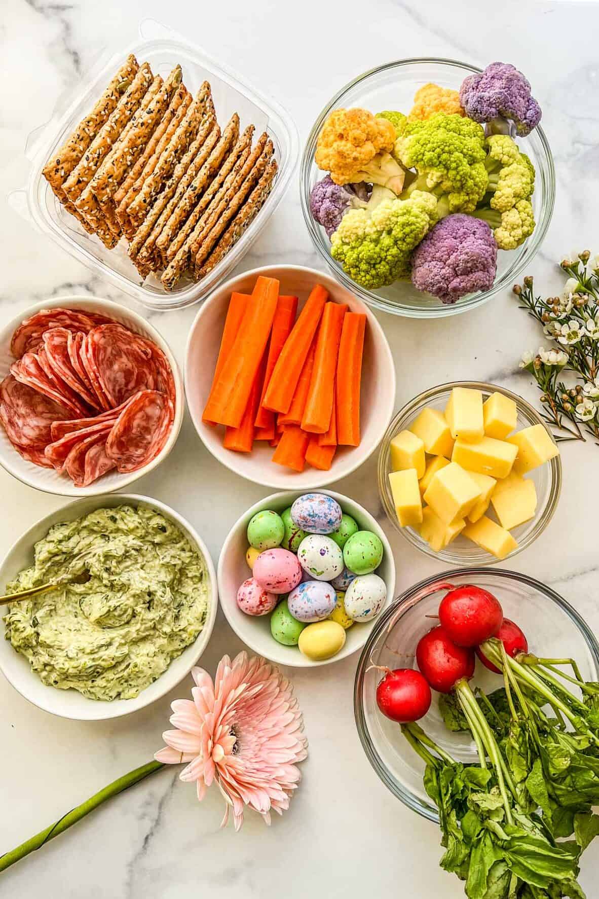 Crackers, cauliflower, carrots, salami, cheese, candy, dip, flowers, and radishes.