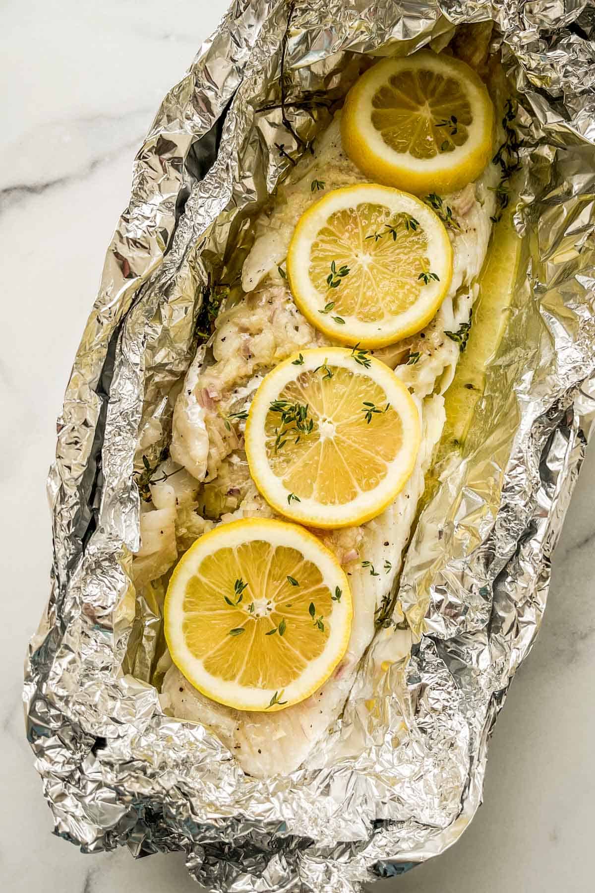 Grilled cod in foil on a marble backdrop.