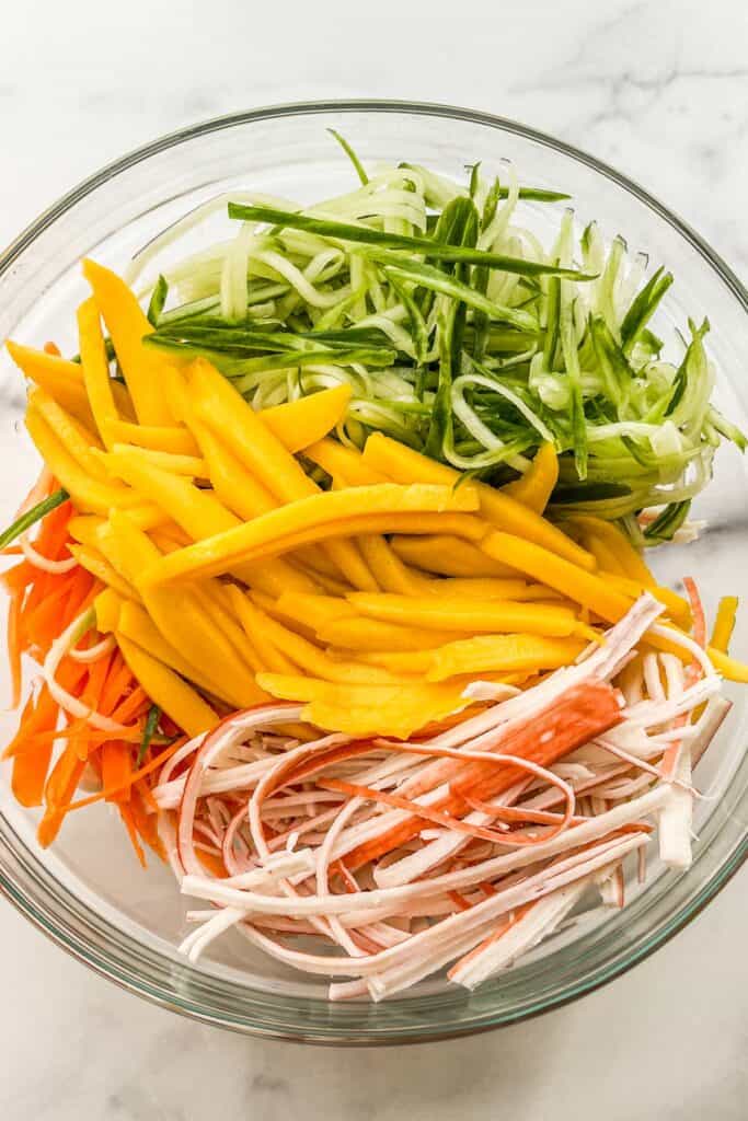 Sliced mangoes, cucumber, crab sticks, and carrots in a mixing bowl.