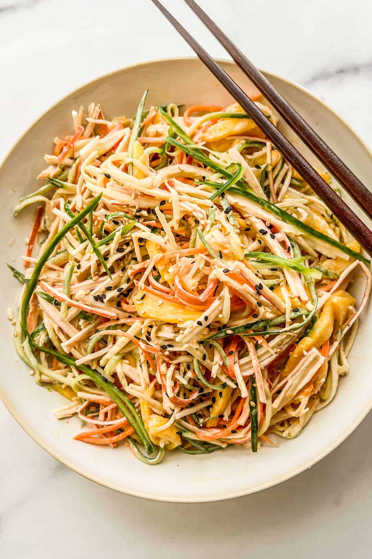 Kani salad with mango in a small serving bowl with wooden chopsticks.