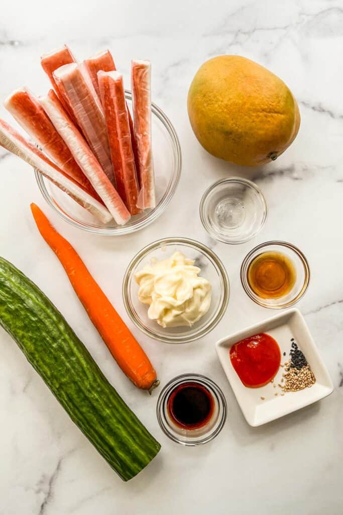 Crab sticks, mango, mayo, a carrot, a cucumber, sesame oil, sriracha, sesame seeds, and soy sauce.