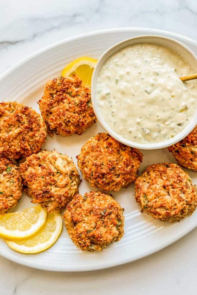 Oven baked crab cakes on a platter with sauce.