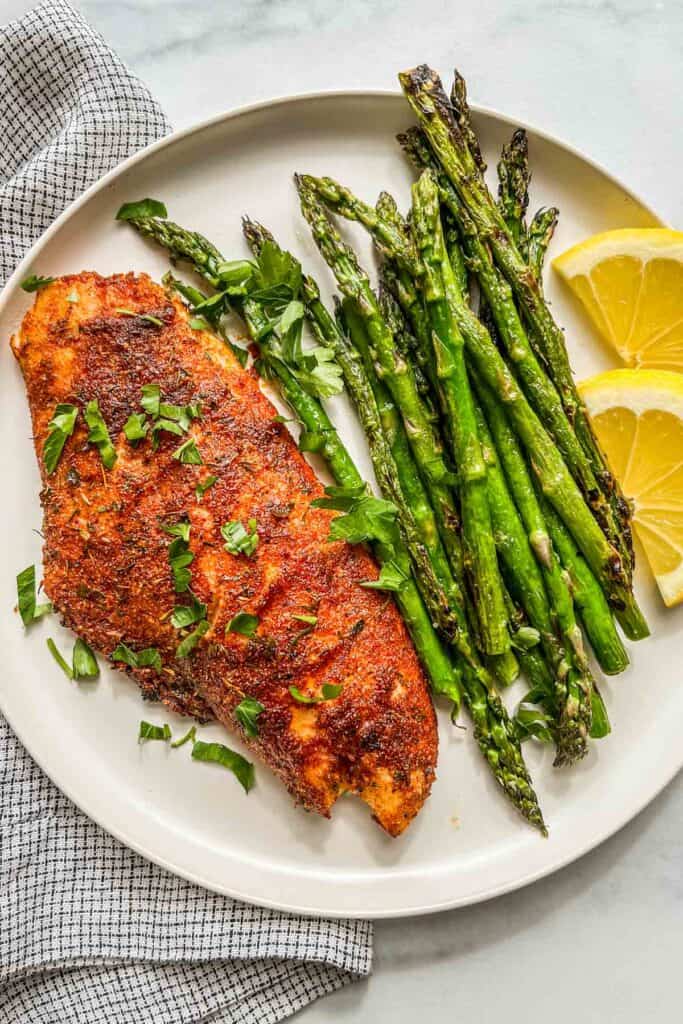 Grilled red snapper on a plate next to asparagus and sliced lemons.