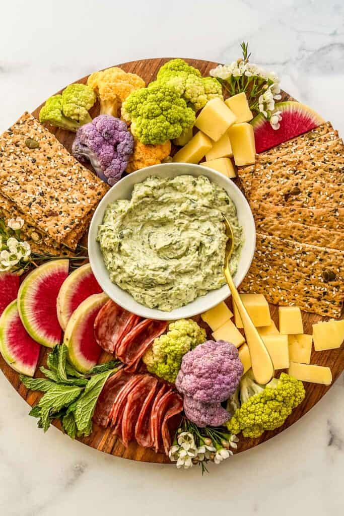 A spring charcuterie board with radishes, salami, crackers, dip, cheese, and veggies.