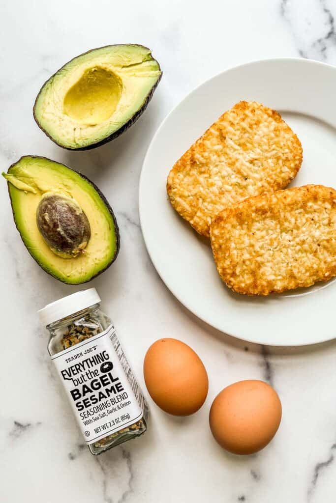 Two hash browns, a halved avocado, two eggs, and everything but the bagel seasoning.