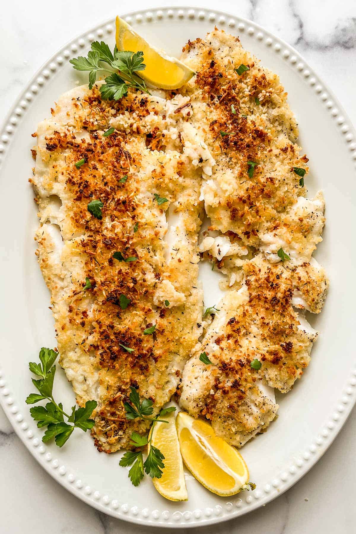 Parmesan panko breaded cod on a serving platter with lemon and parsley.