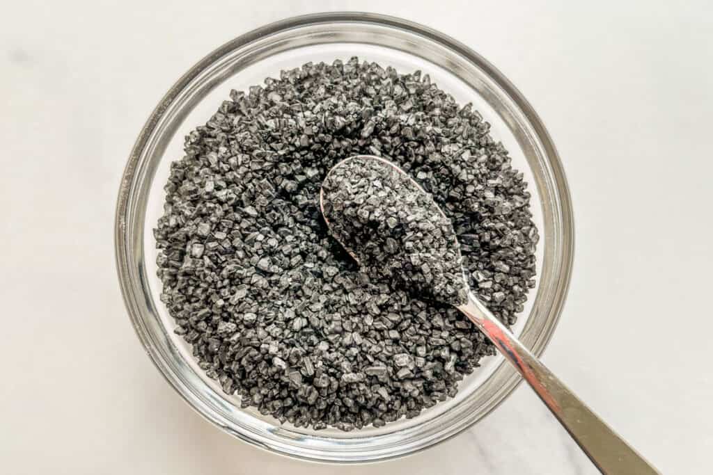 Black lava salt in a small glass bowl with a spoon.