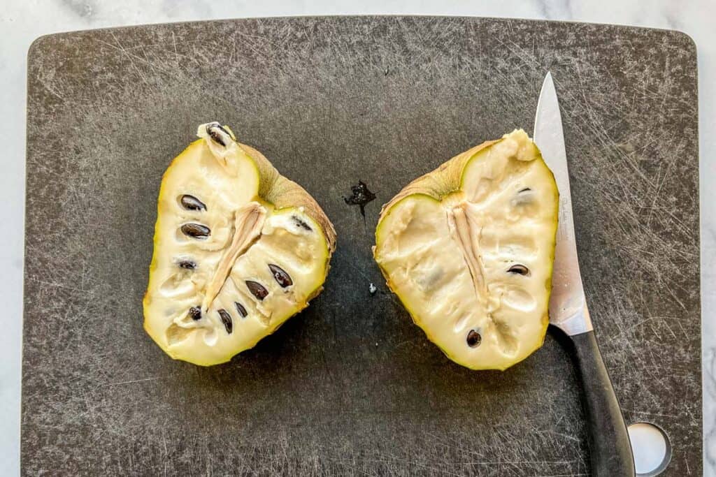 A cherimoya cut in half on a black cutting board.