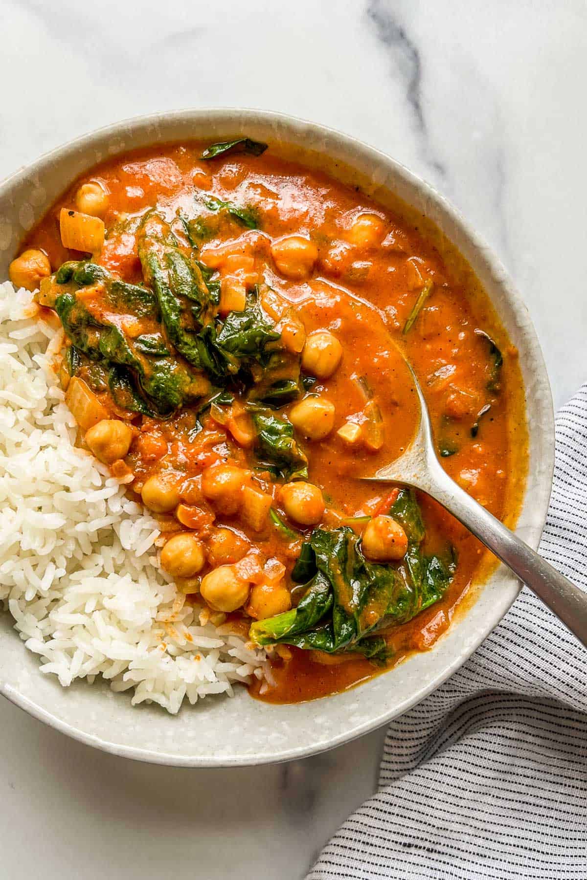 Chickpea spinach curry with rice in a bowl with a spoon.