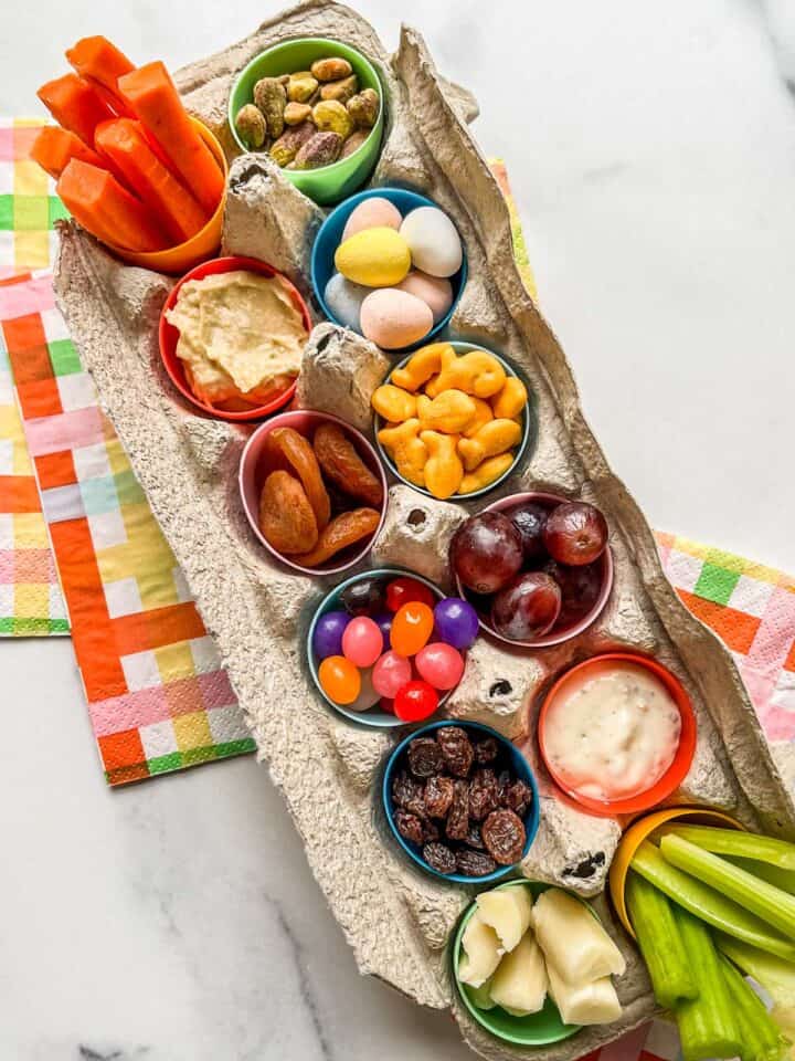 An egg tray with plastic eggs, filled with snacks for kids.