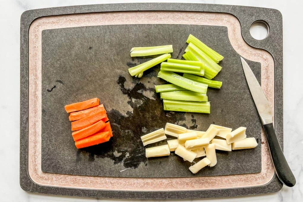 Cut celery sticks, carrot sticks, and mozzarella sticks on a black cutting board.