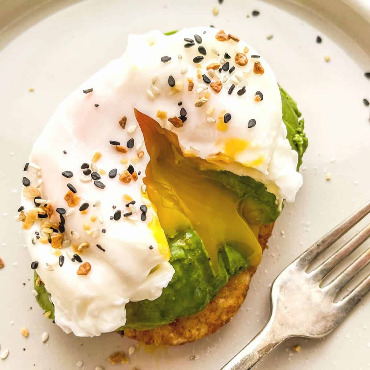 A poached egg, cut open, on top of avocado and a hash brown patty.