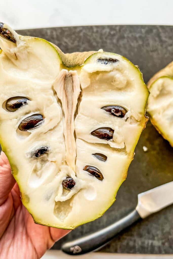 A halved cherimoya being held in a hand.