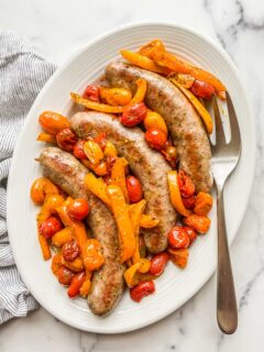 Baked Italian sausage with peppers and tomatoes on a serving plate.