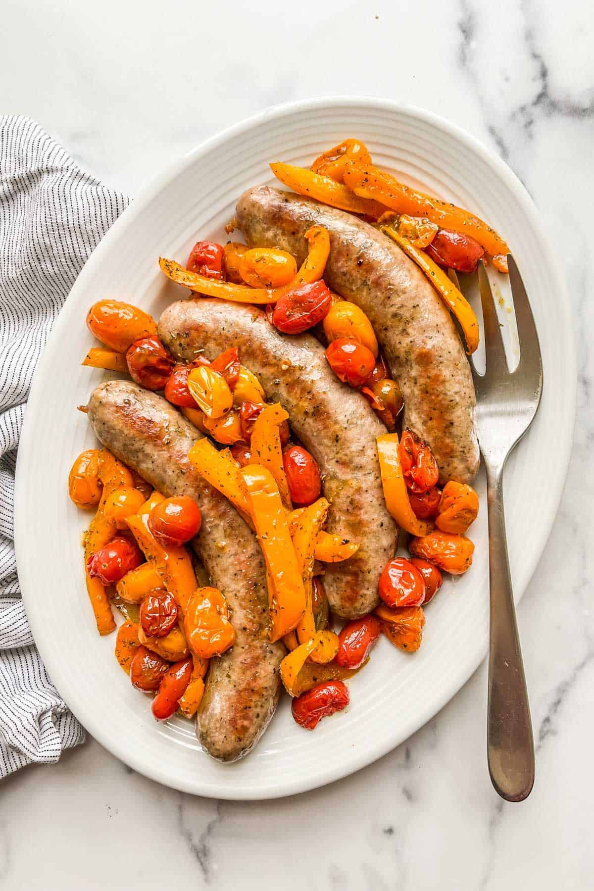 Baked Italian sausage with peppers and tomatoes on a serving plate.