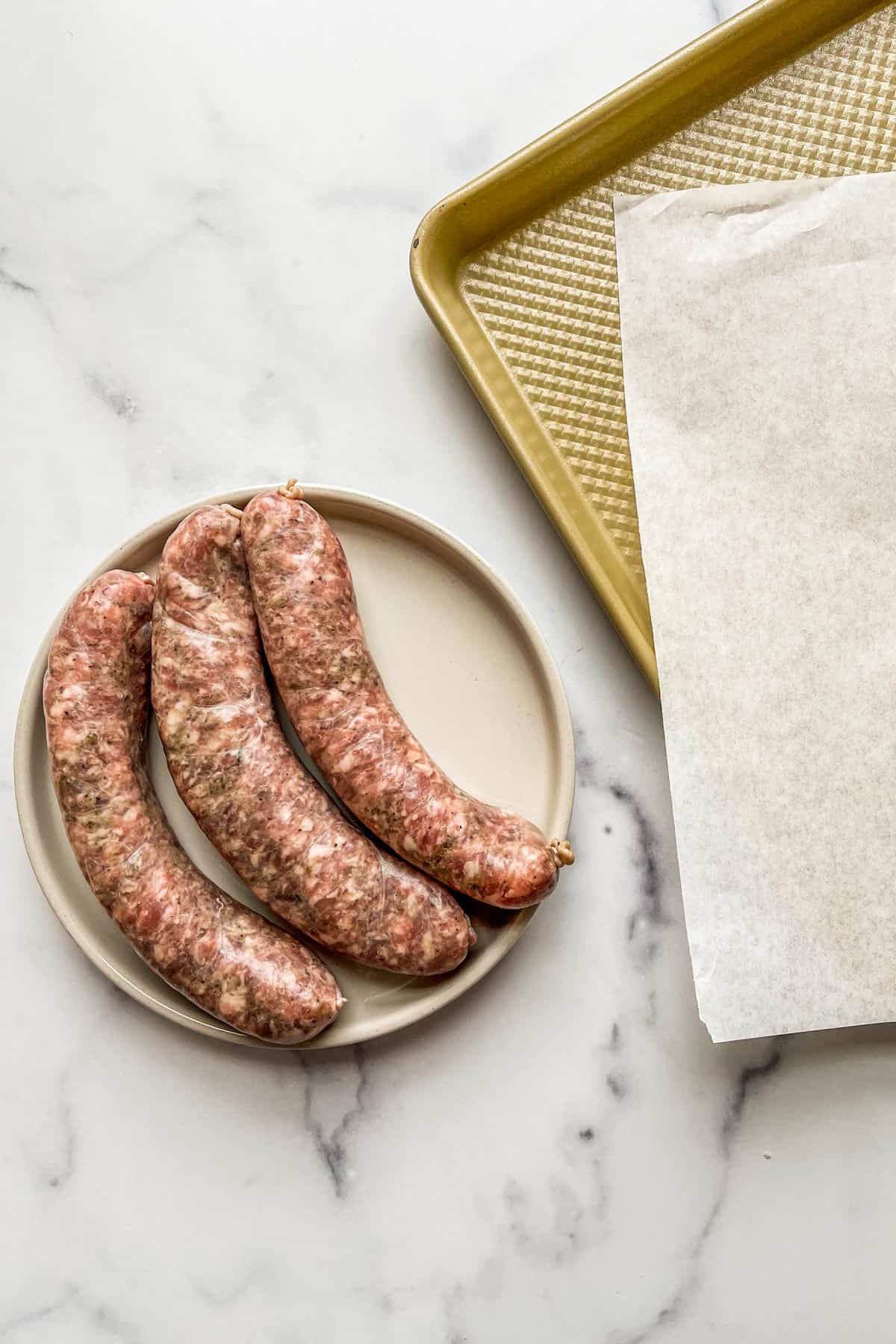 Italian sausage on a plate next to a baking sheet and parchment paper.