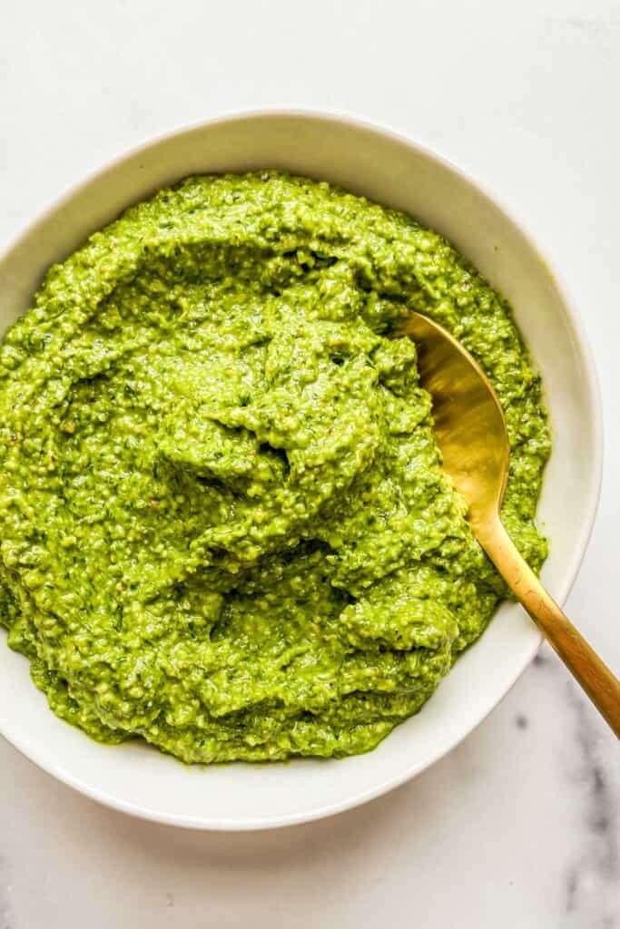 Ramp pesto in a white bowl with a gold spoon.