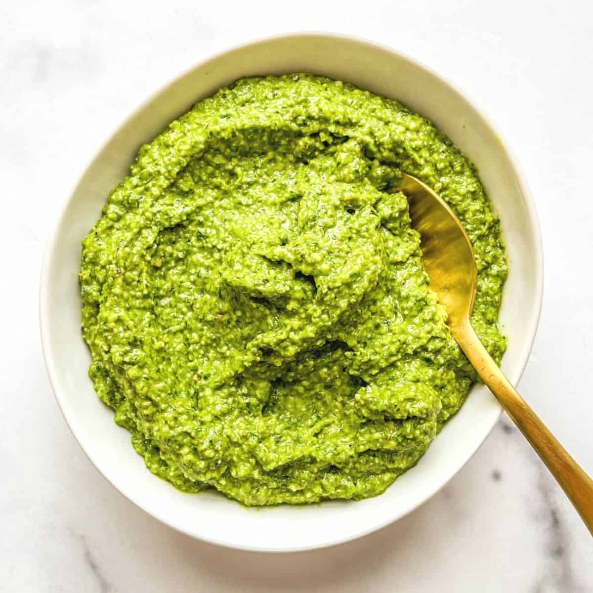Ramp pesto in a white bowl with a gold spoon.