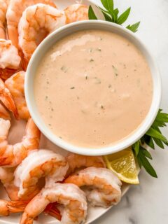 A bowl of seafood sauce next to shrimp.
