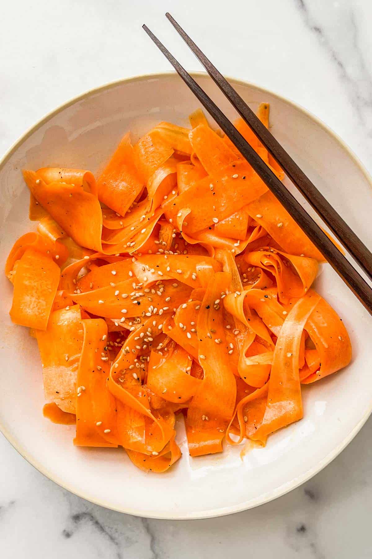 A bowl of shaved carrot salad with chopsticks resting on it.