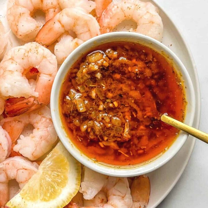 Cajun butter seasoning for seafood in a small bowl with a spoon, next to shrimp.