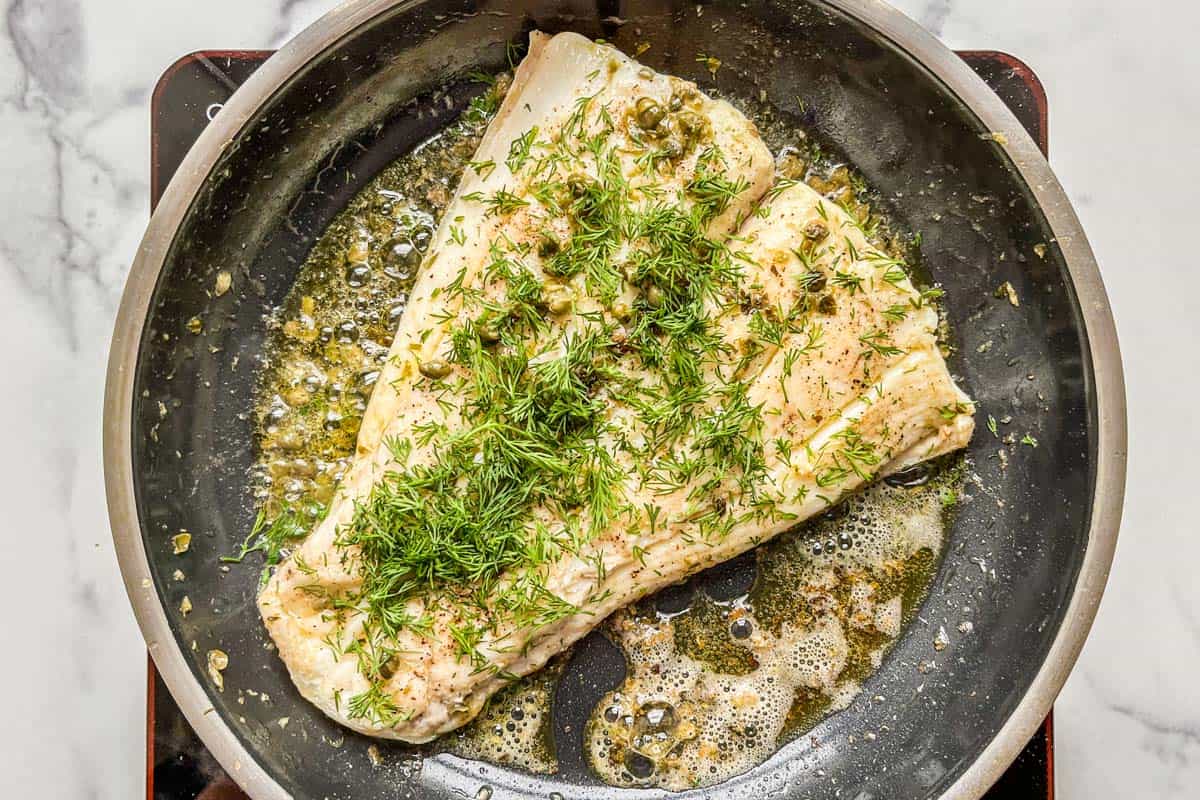 Pan seared halibut with dill and capers in a skillet.