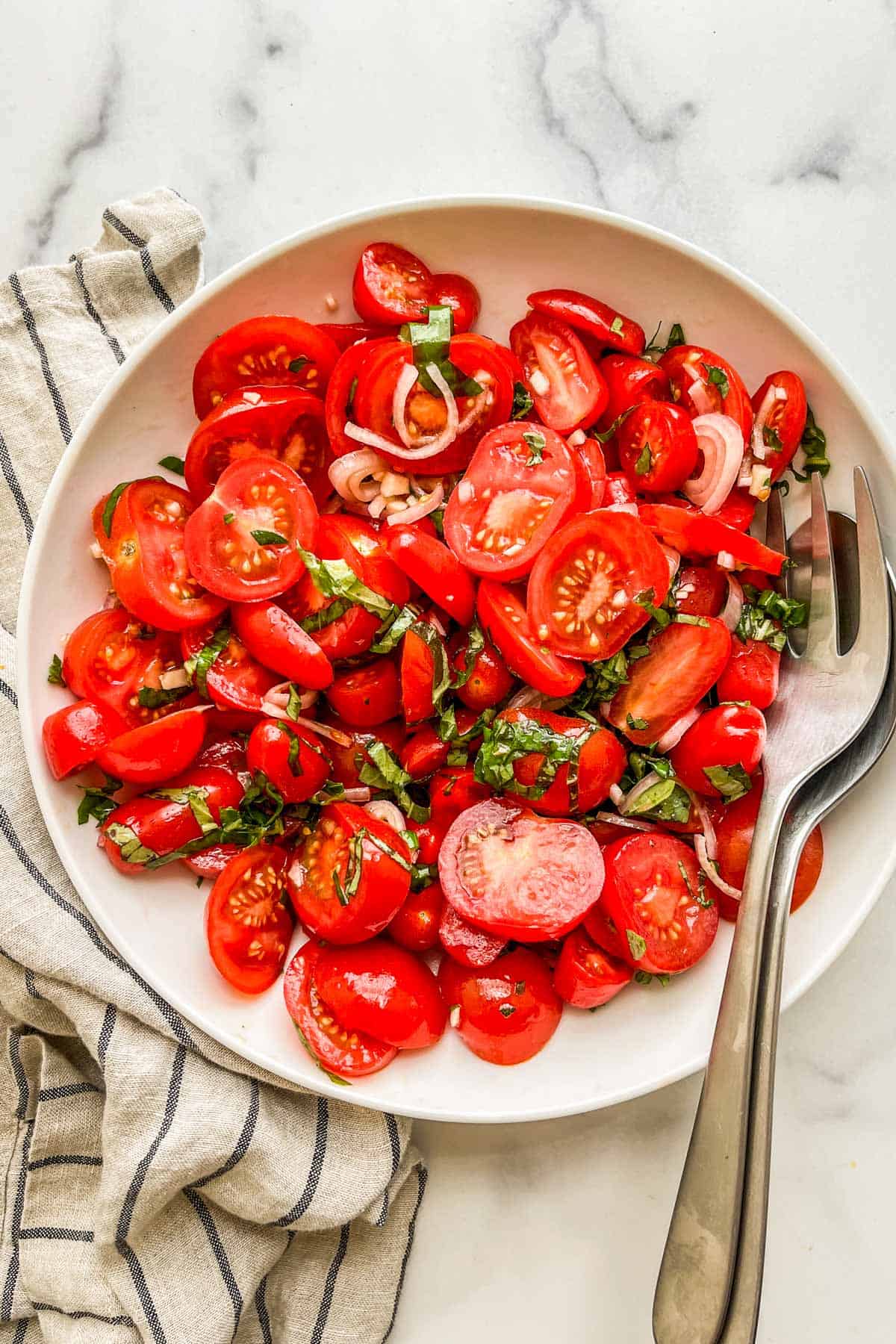 Italian tomato salad in a large white serving bowl with serving utensils.