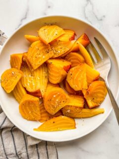 Roasted golden beets in a white bowl with a serving fork.