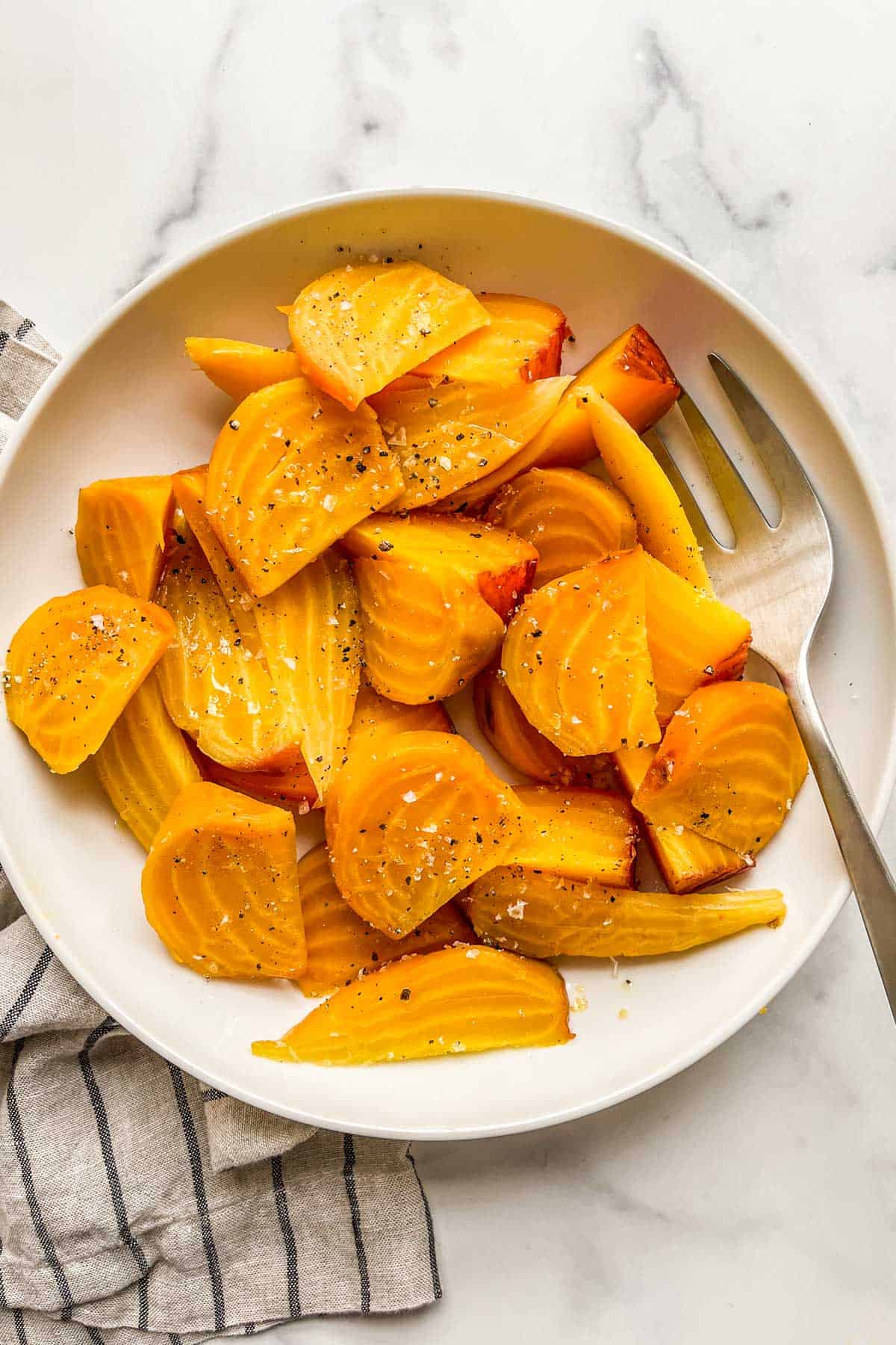 Roasted golden beets in a white bowl with a serving fork.