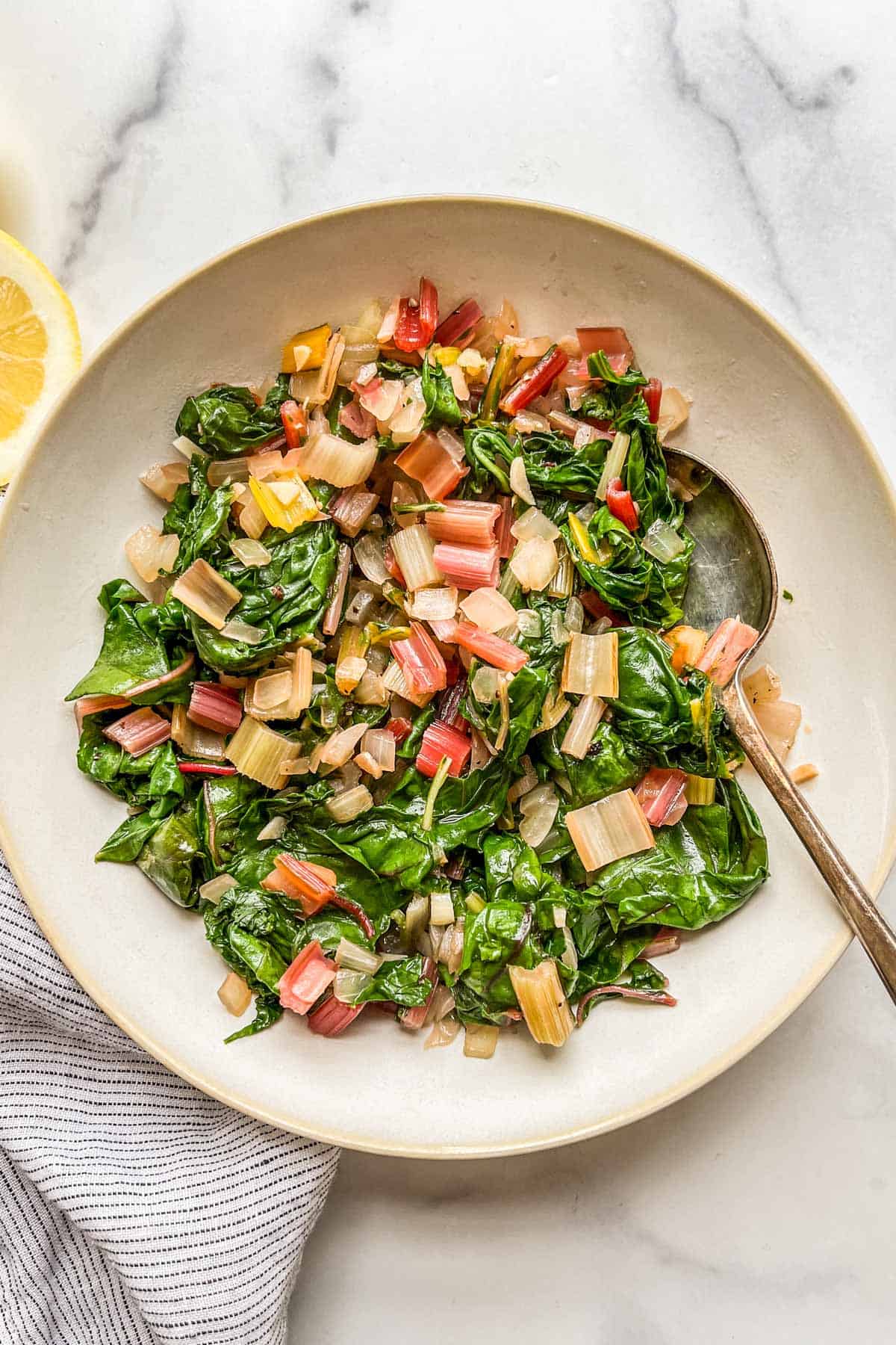 Sauteed swiss chard in a white serving bowl with a spoon.