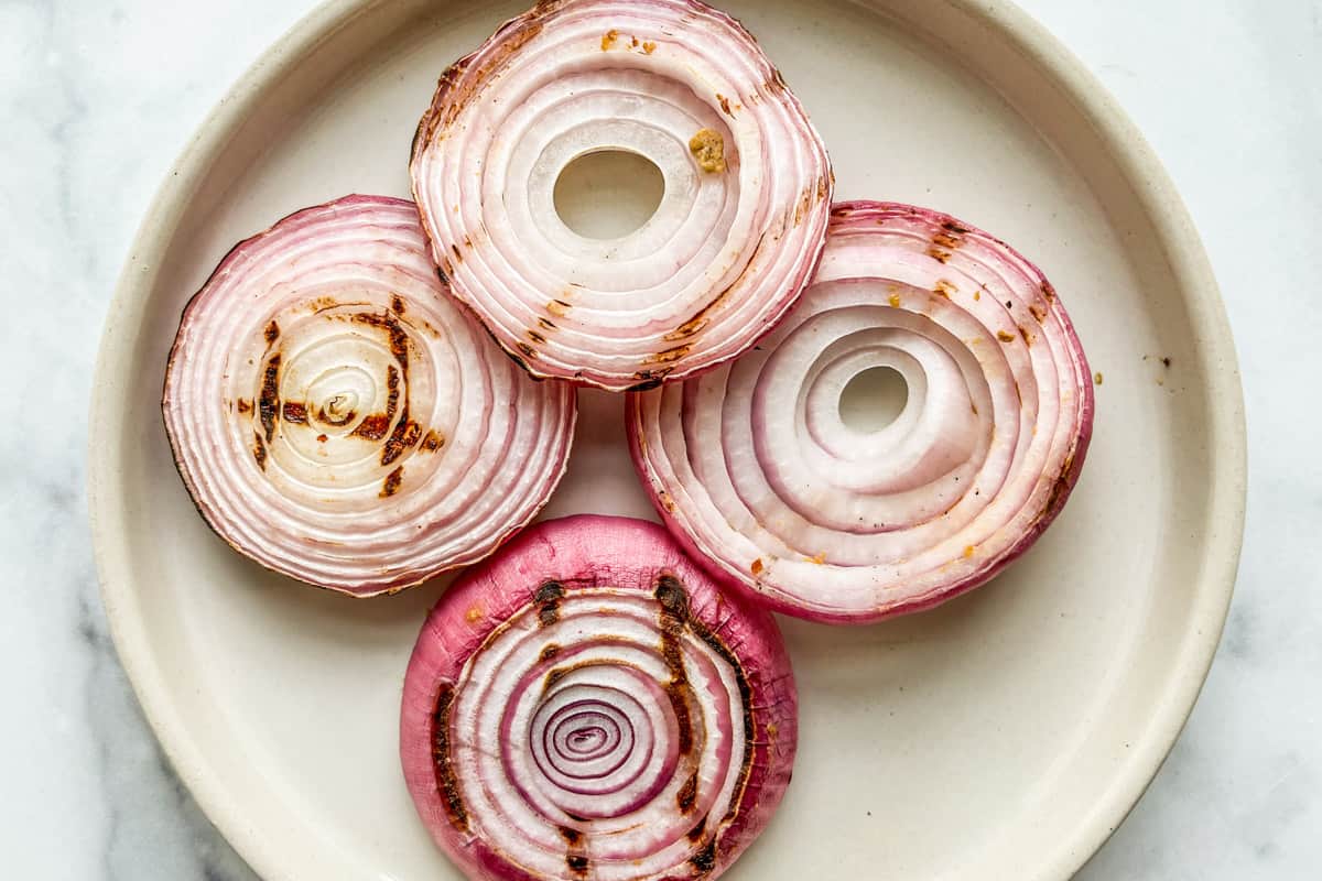 Four slices of grilled red onion on a plate.